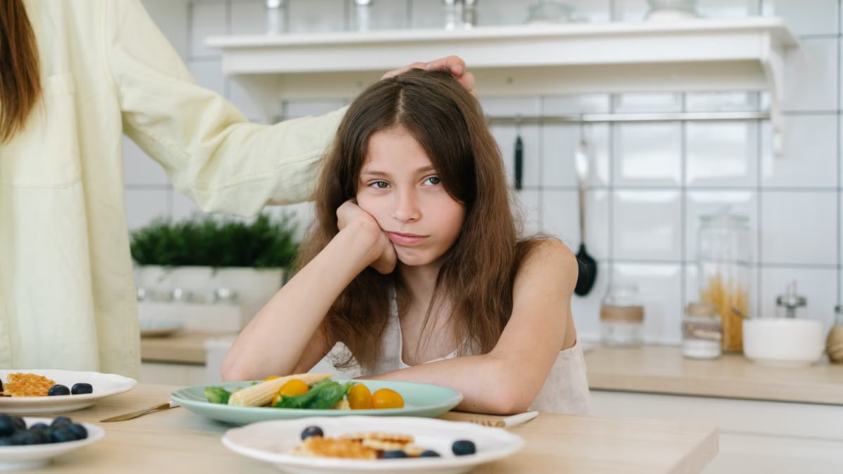 Young girl looking displeased with breakfast in a home kitchen setting.